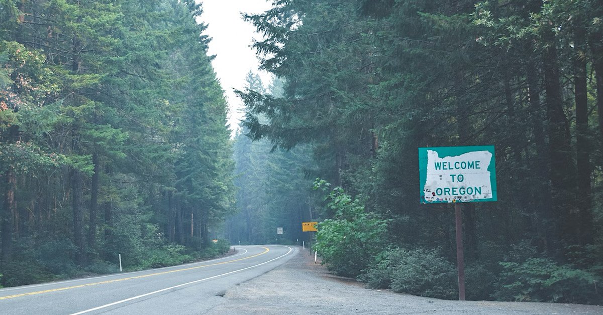 Welcome to oregon sign with road surrounded by trees